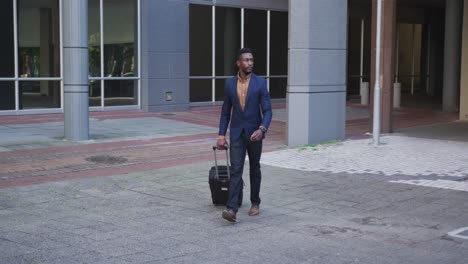 african american businessman walking with suitcase in city street