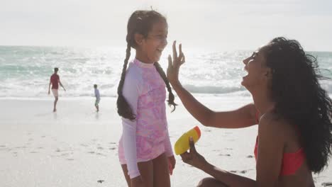 Happy-hispanic-mother-applying-sun-cream-on-daughter-face-on-beach