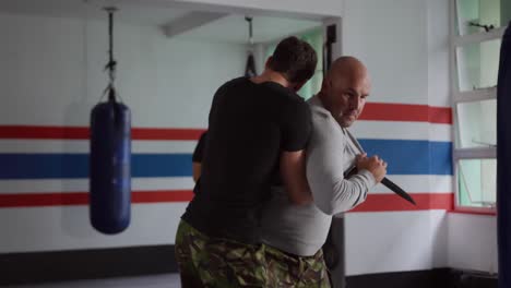 hombre caucásico aprendiendo autodefensa del entrenador en el gimnasio