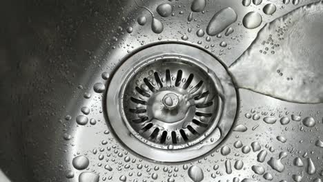 agua del grifo corriendo por el desagüe y salpicando en el fregadero de la cocina de acero inoxidable tiro de cerca