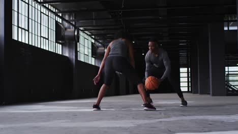 african american man and woman standing in an empty building playing basketball