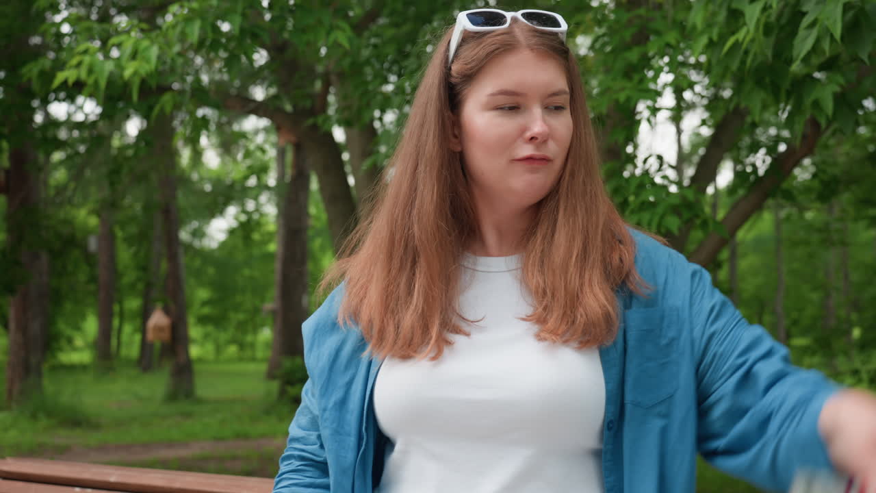 무성한 녹색 나무로 둘러싸인 공원에서 춤을 추며 자유, 기쁨, 에너지를 자연광 아래에서 표현하는 행복한 여성이 캐주얼한 옷을 입고 밝게 웃고 있어요.