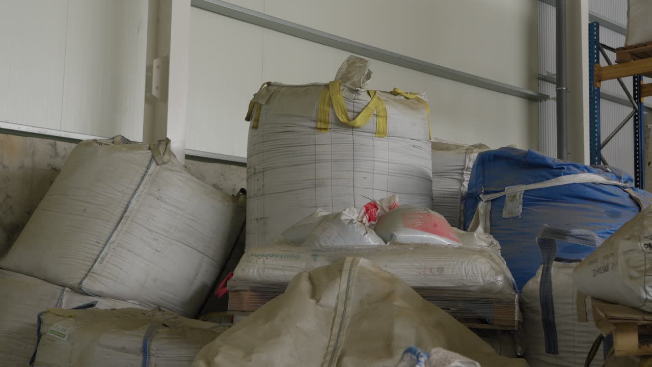 Multiple large bulk bags filled with shredded plastic flakes stacked inside recycling facility warehouse