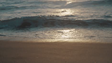 small waves from the pacific ocean roll out onto a beautiful brown sand beach as the setting sun settles on the water