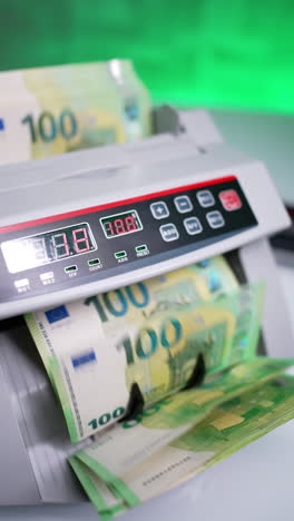 money stack placed into cash counting machine. one hundred euro bills in a bank device. close up. vertical video.