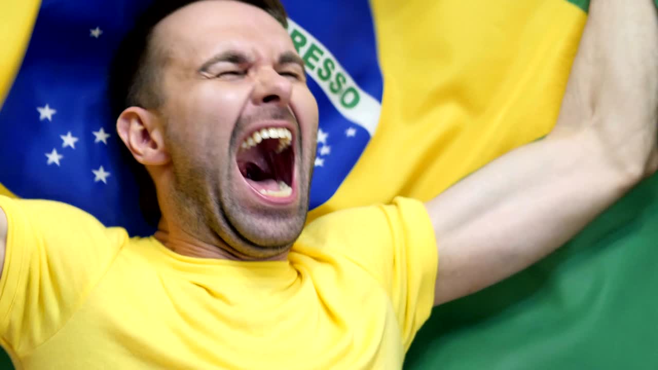 fanático brasileño celebrando mientras sostiene la bandera de brasil en cámara lenta, 4k, de alta calidad