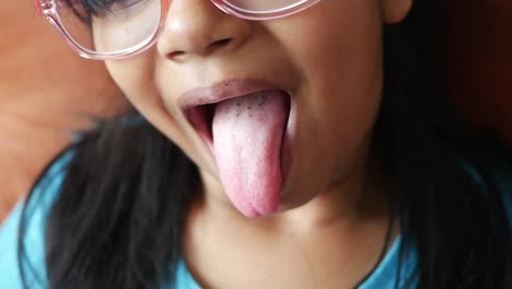 a young girl with glasses sticks her tongue out