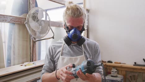 caucasian male surfboard maker wearing a face mask and making a surfboard