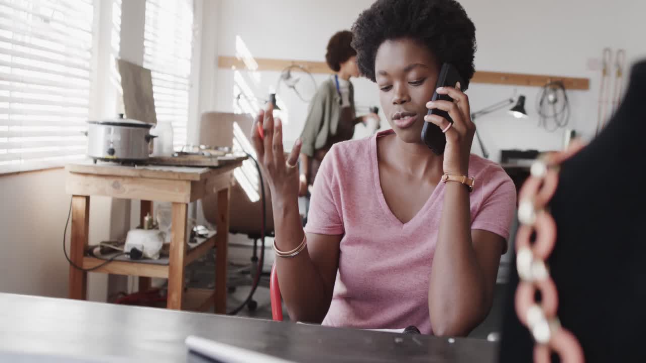 Travl afroamerikansk kvindelig medarbejder taler i smartphone i smykkestudie i slow motion.