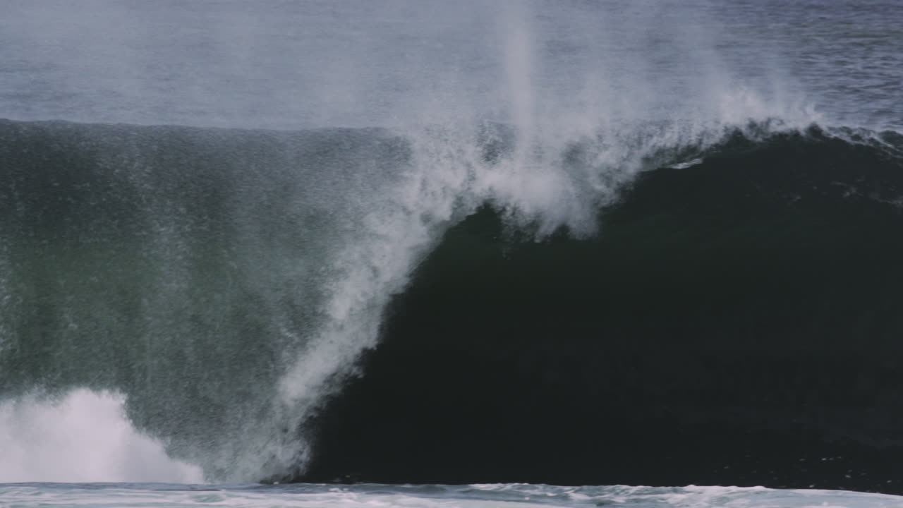 Slow motion wave collapses under itself sending spray outward, captured close-up in dramatic detail
