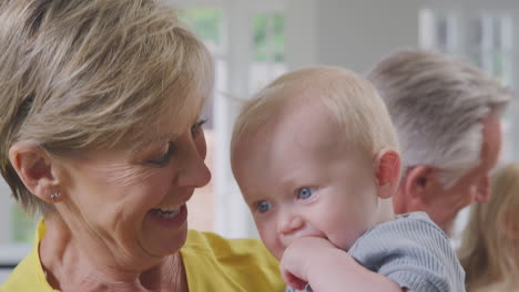 grandmother looking after and playing with laughing baby grandson sitting at kitchen table