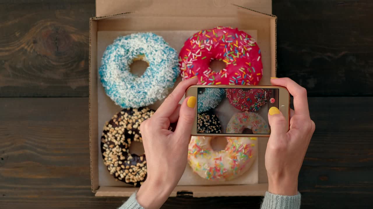 las manos de la mujer toman fotos con el teléfono inteligente de deliciosas rosquillas en la caja