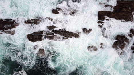 aerial climbing top down view of rough sea waves hitting coastal rock formation