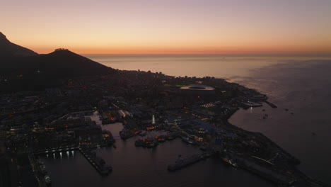 Atemberaubende-Panoramaaufnahmen-Aus-Der-Luft-Von-Der-Uferpromenade-Mit-Jachthafen-Und-Unterhaltungsviertel-In-Der-Dämmerung.-Kapstadt,-Süd-Afrika