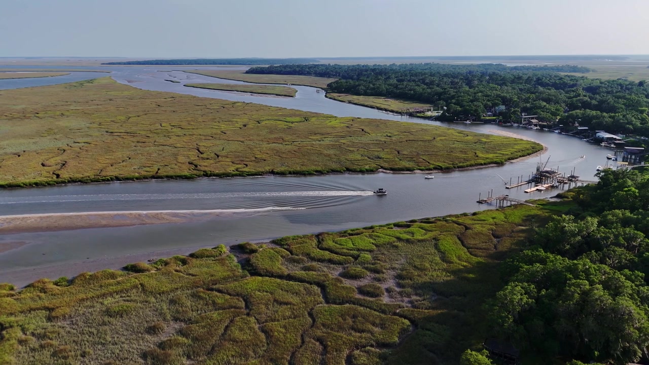 Filmato aereo 4K con drone di un motoscafo che naviga attraverso corsi d'acqua tortuosi e rigogliose paludi salmastre a Shellman Bluff, Georgia, durante una giornata di sole