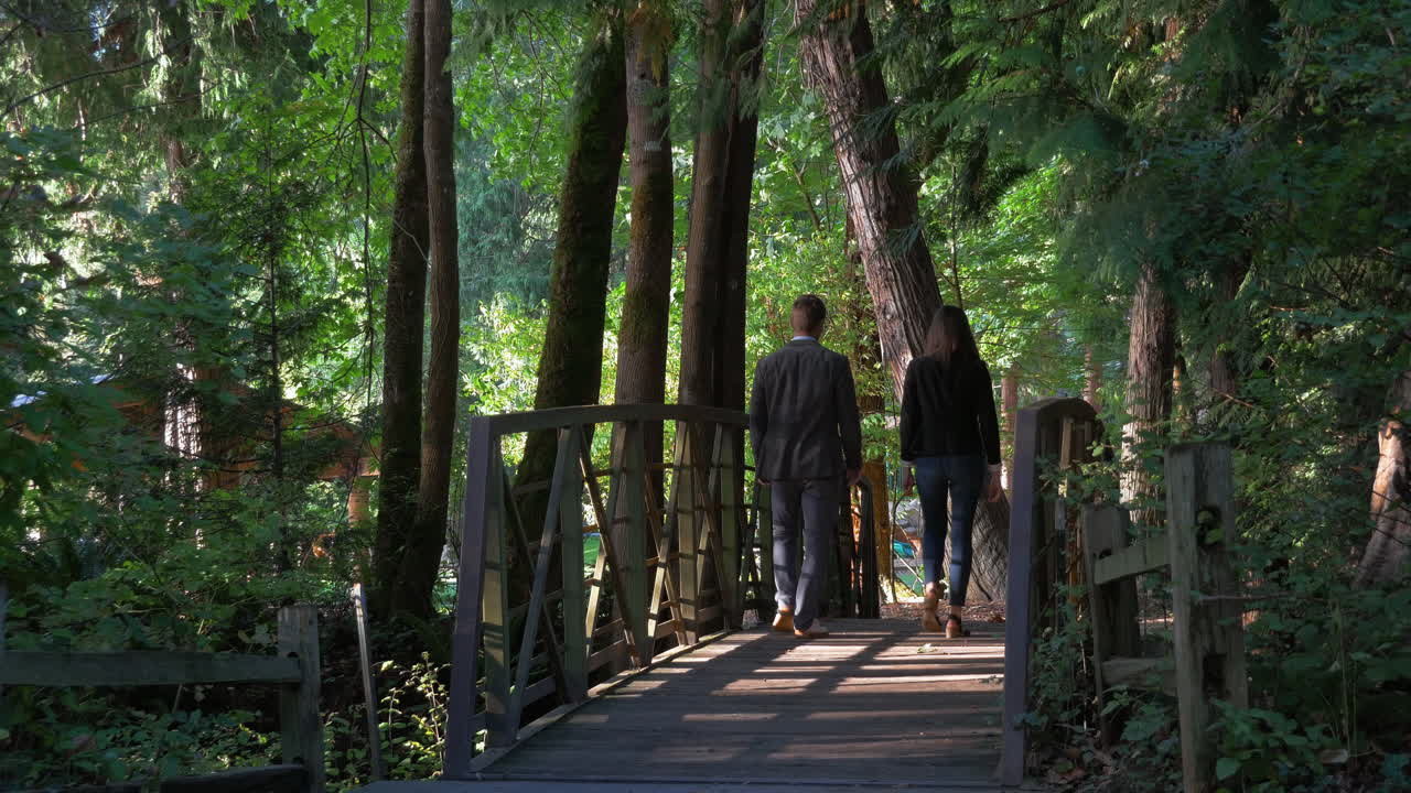 Savvy young, good looking business professionals walk away from camera in a park over a beautiful shaded wooden bridge outside in nature on a sunny day