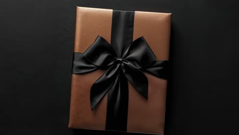 a gold gift box with a black ribbon and bow