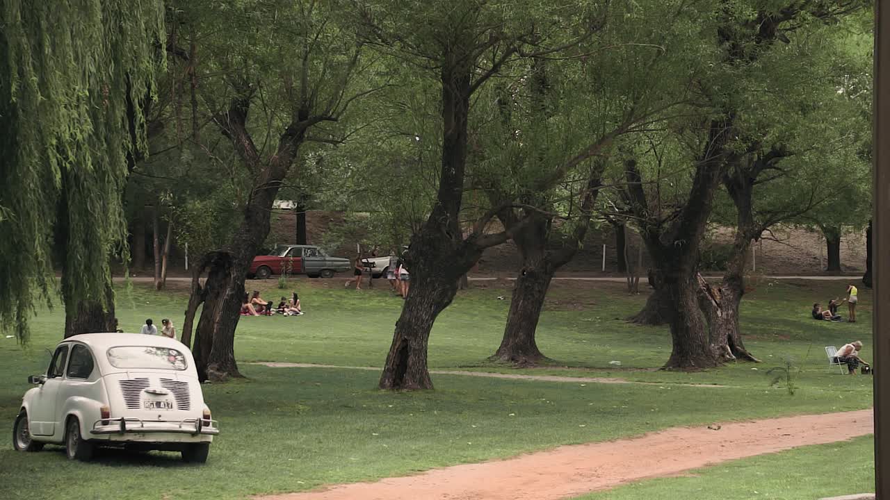 Gimbal shot of people in park and old Fiat parked on grass. Cordoba, Argentina