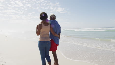 feliz pareja afroamericana caminando y abrazándose en una playa soleada
