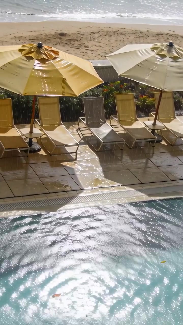 Vertical video: Showing breeze stirring pool ripples, leaves drifting by chairs at poolside
