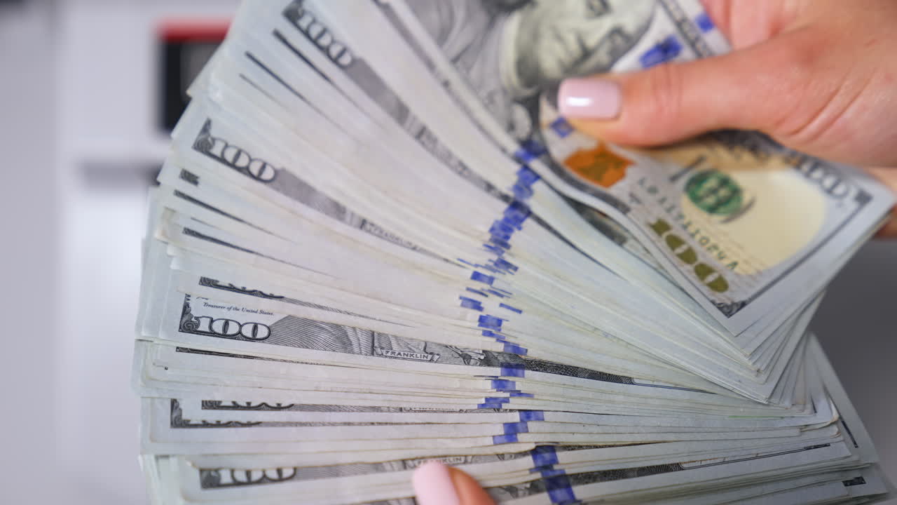 Usa money in woman's hands. Wad of one hundred dollar banknotes in hands on blur background of automatic counter machine. Finance concept. Close-up.