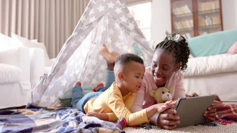 Happy-african-american-sister-and-brother-using-tablet-and-smiling-at-home,-slow-motion