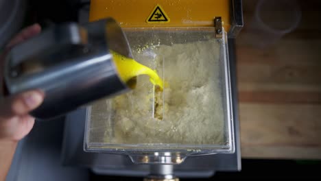 close up view in slow motion of a chef adding liquid ingredients to a pasta dough maker machine in a restaurant,