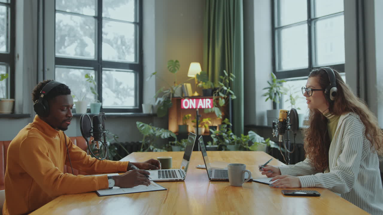 두 명의 다민족 캐스터가 스튜디오에서 함께 오디오 콘텐츠를 녹음합니다.