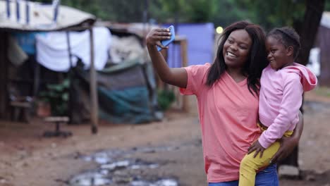 black african lesbian woman holding her cute daughter taking a selfie in an informal settlement slum