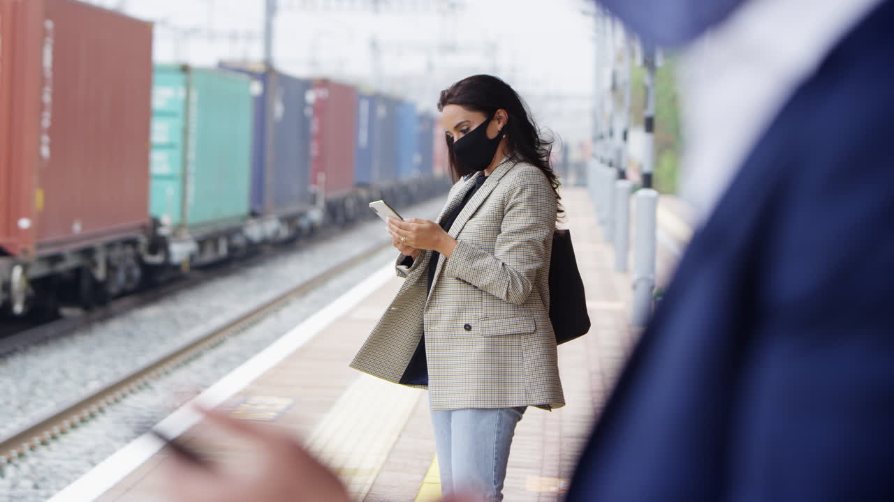 Pendolari d'affari sulla piattaforma ferroviaria con telefoni cellulari che indossano maschere protettive durante la pandemia