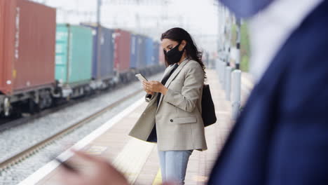 geschäftsreisende auf dem bahnsteig mit mobiltelefonen und ppe-gesichtsmasken während der pandemie