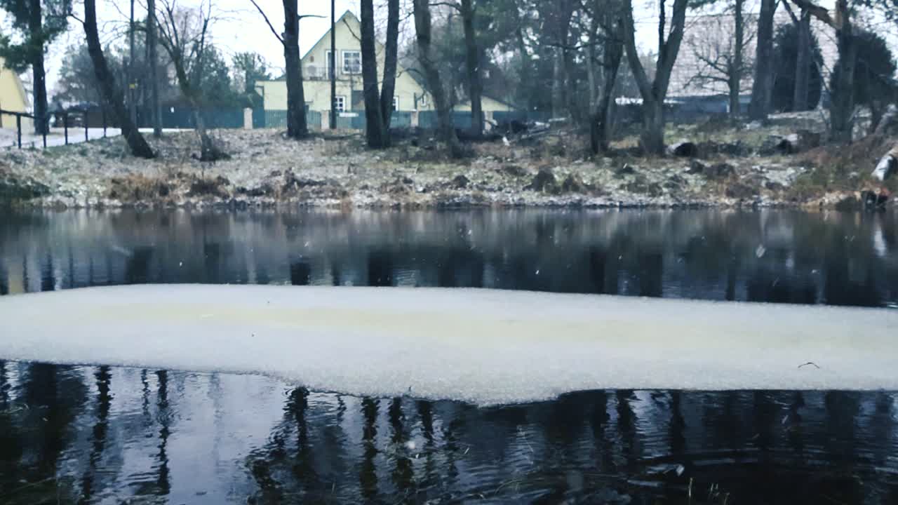 겨울철에 어두운 강이나 호수 물의 화려한 낮은 각도 영상으로 은 얼음 층이 떠다니는 동안 겨울 눈이 반사되는 물에 느린 속도로 떨어지면서 파동됩니다.