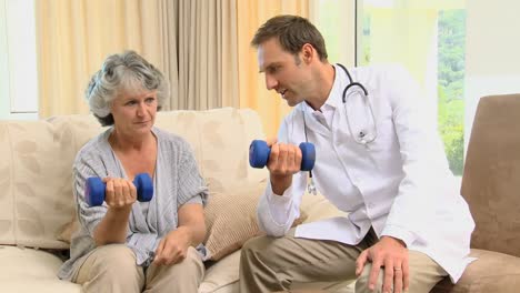 Joven-Médico-Mostrando-A-Su-Viejo-Paciente-El-Uso-De-Pesas