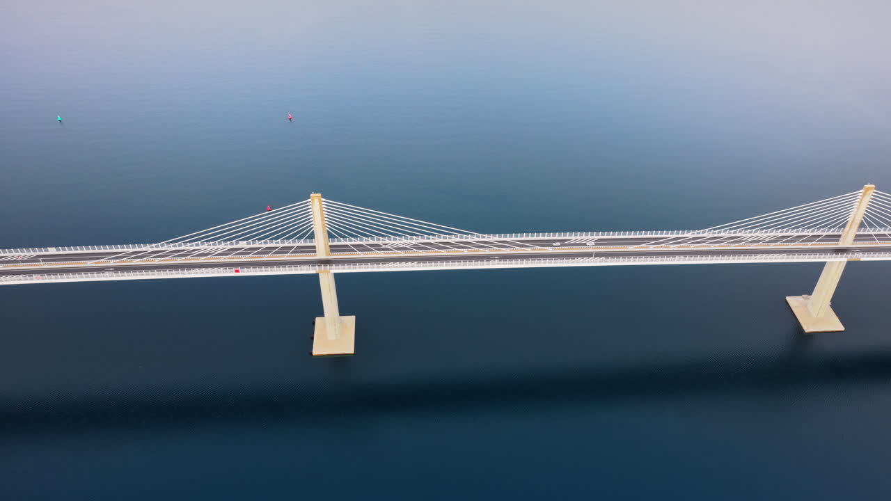 Aerial drone view of the Peljesac Bridge near Komarna, Croatia, partially shrouded in low coastal fog with mountains in the background