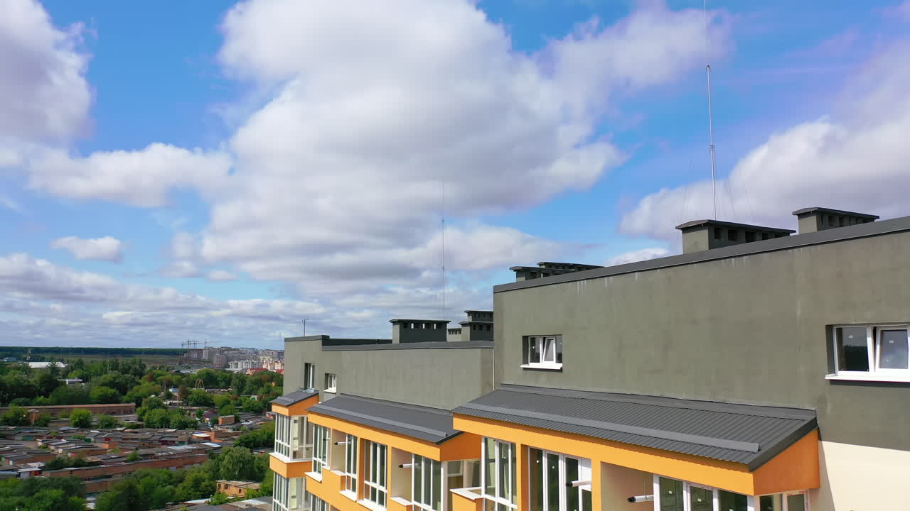 Modern architecture in the city. Tall building with grey roof in the city. New residential apartment building under blue sky. Camera rising.