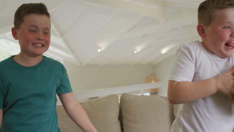 happy caucasian boy with brother watching tv and holding football in living room