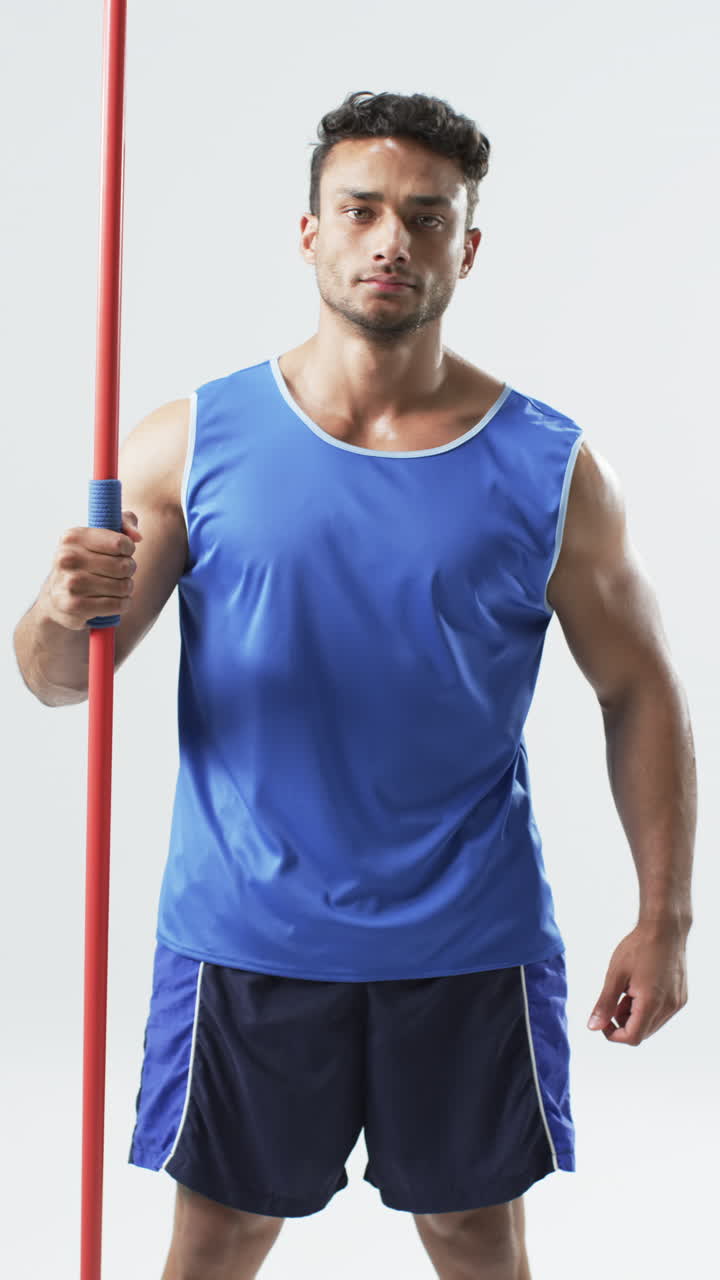 Vertical video: Biracial male athlete holding red pole, white background
