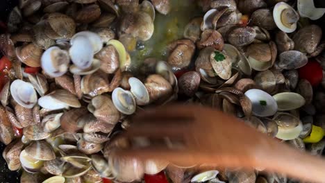 stirring delicious fresh shell clams with parsley peppers and tomatoes with wooden forks in hot pan