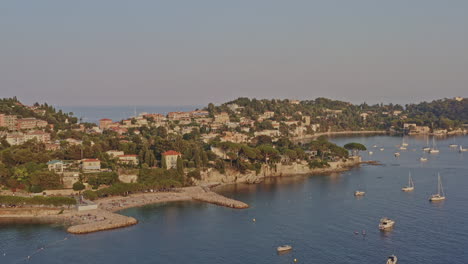 Villefranche-sur-Mer-France-Aerial-v5-pan-shot-capturing-beautiful-small-secluded-beaches-and-seafront-residential-buildings-and-resorts,-with-sailboats-cruising-on-mediterranean-sea---July-2021