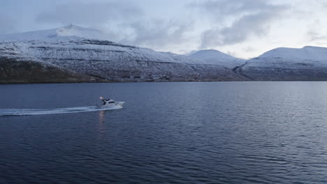 faroe islands, 4k aerial tracking three quaeter shot of fishing boat with snow covered mountains in the background