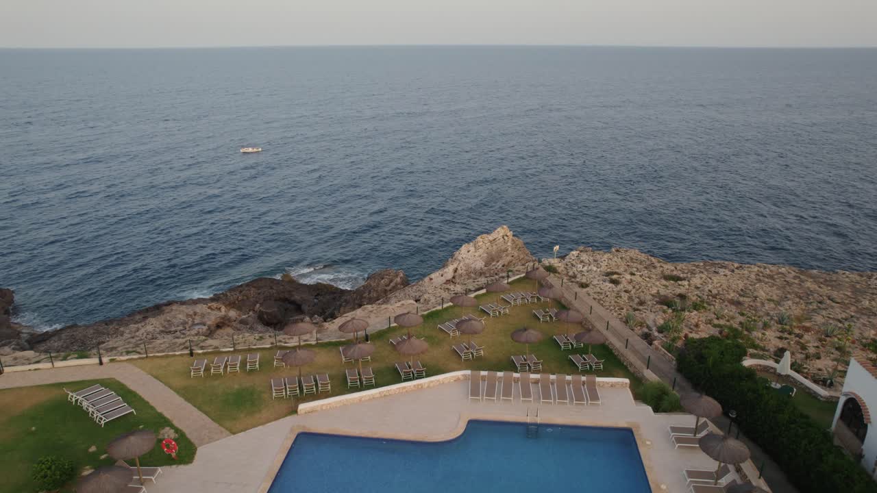 drone volando sobre resort privado en mallorca, españa al atardecer con propiedad de lujo en el borde del acantilado y piscina vacía