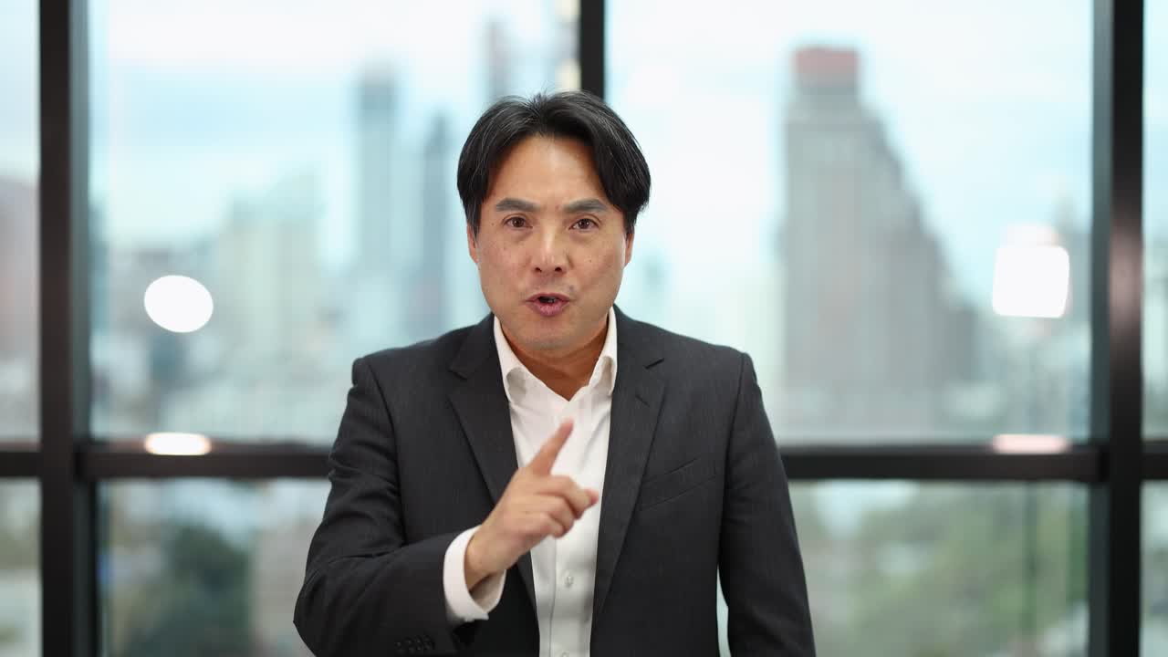 Confident businessman signals silence, then calms, in bright office with cityscape background, steady camera