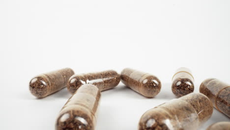 close-up of brown herbal supplements in clear capsules scattered on white