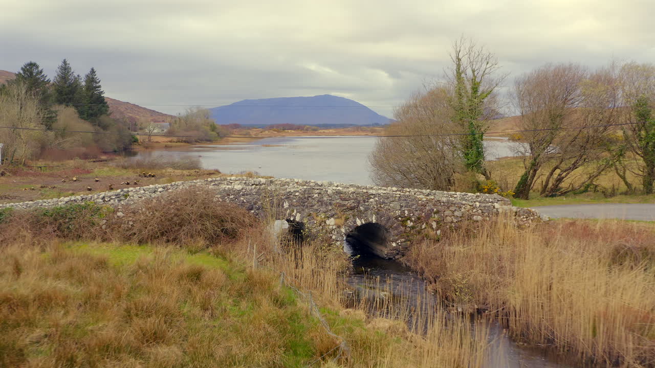 Retreating drone shot of iconic Quiet Man stone bridge showcasing surrounding Connemara countryside