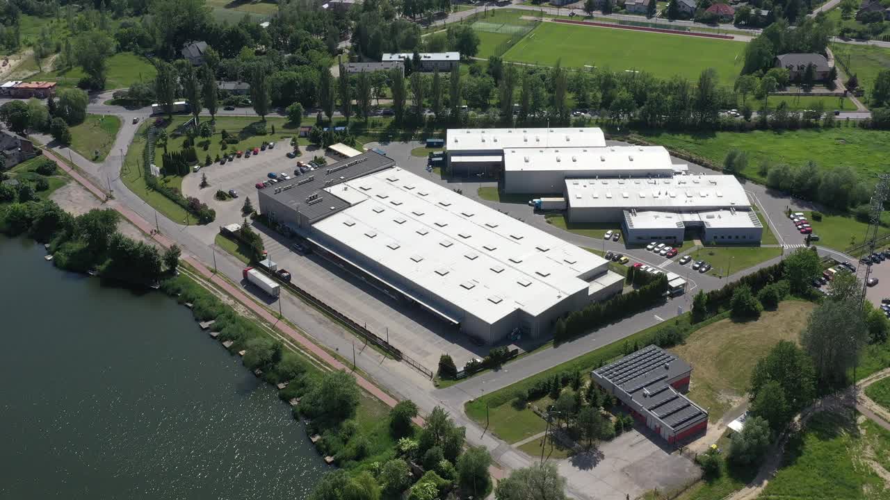 Inquadratura aerea laterale in movimento di un molo di carico/scarico di un magazzino industriale dove molti camion con semirimorchi caricano e scaricano merci