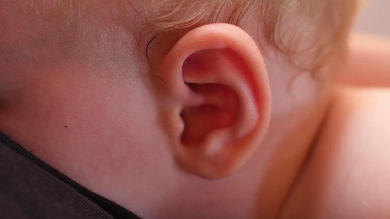 Dettaglio ravvicinato dell'orecchio di un neonato durante l'allattamento, che cattura la cura intima, il comfort del bambino e il delicato legame materno in un tranquillo ambiente domestico.