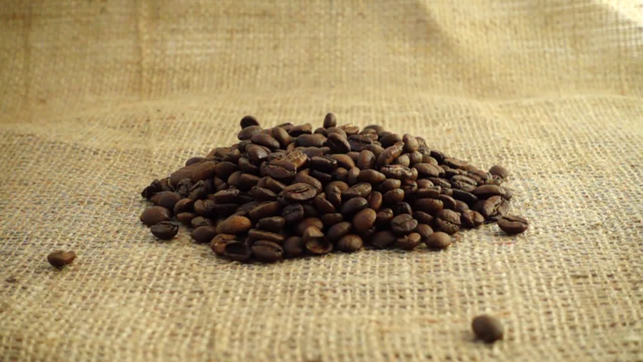 Chicchi di caffè cadono su tela di iuta al rallentatore.