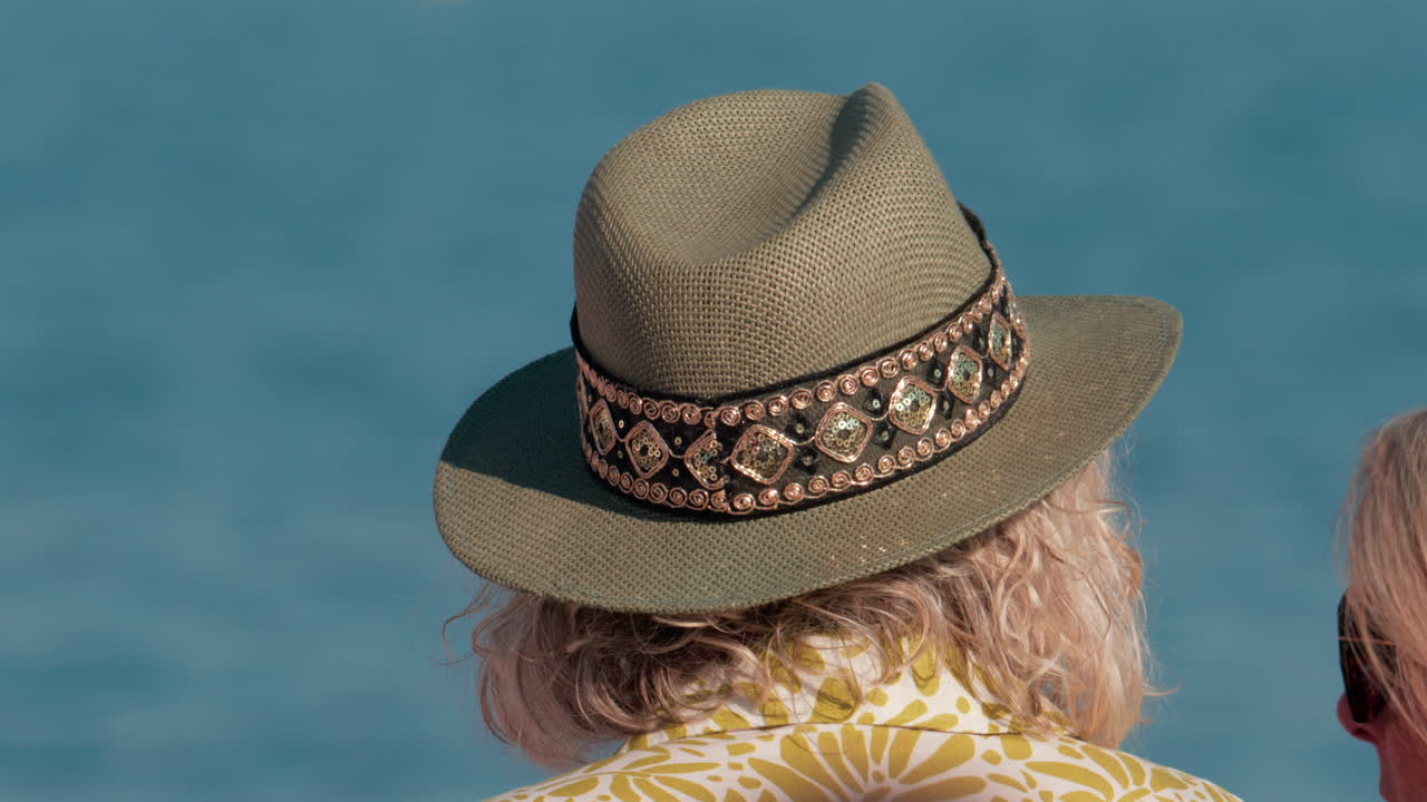 Close up of a decorated sun hat worn by a person facing the calm blue water