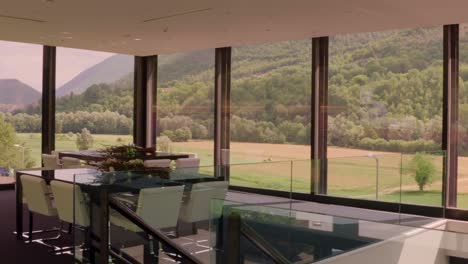 a wide shot pans left, showcasing a modern dining area with white chairs, floral centerpieces, and large windows framing a stunning view of rolling hills and mountains.