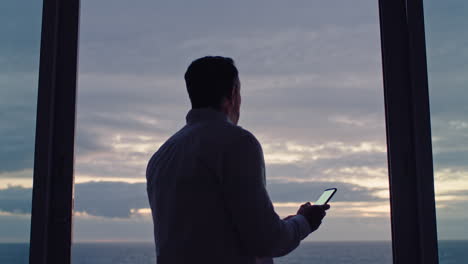 joven usando un teléfono inteligente en una habitación de hotel enviando mensajes de texto compartiendo el estilo de vida de vacaciones en las redes sociales disfrutando de la vista del océano al atardecer